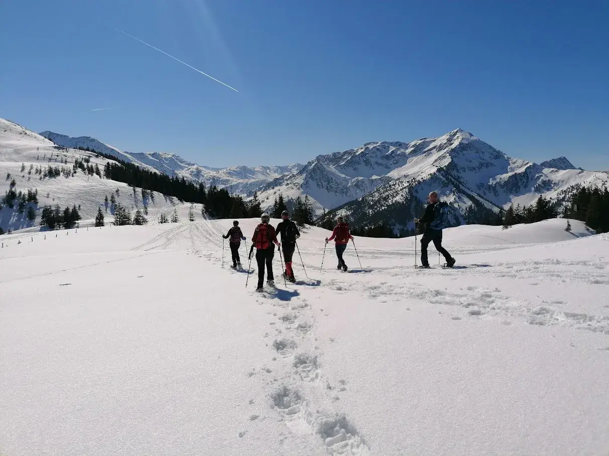 Eine geführte Gruppe beim Schneeschuhwandern durch eine sonnige, tief verschneite Berglandschaft der Kitzbüheler Alpen.