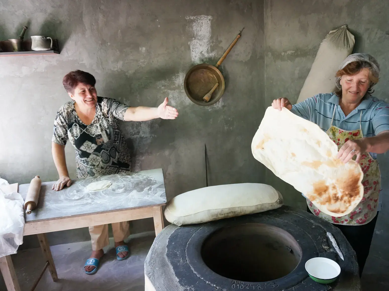 Zwei gastfreundliche armenische Frauen backen traditionelles Lavash-Fladenbrot in einem typischen Tonir-Erdofen.