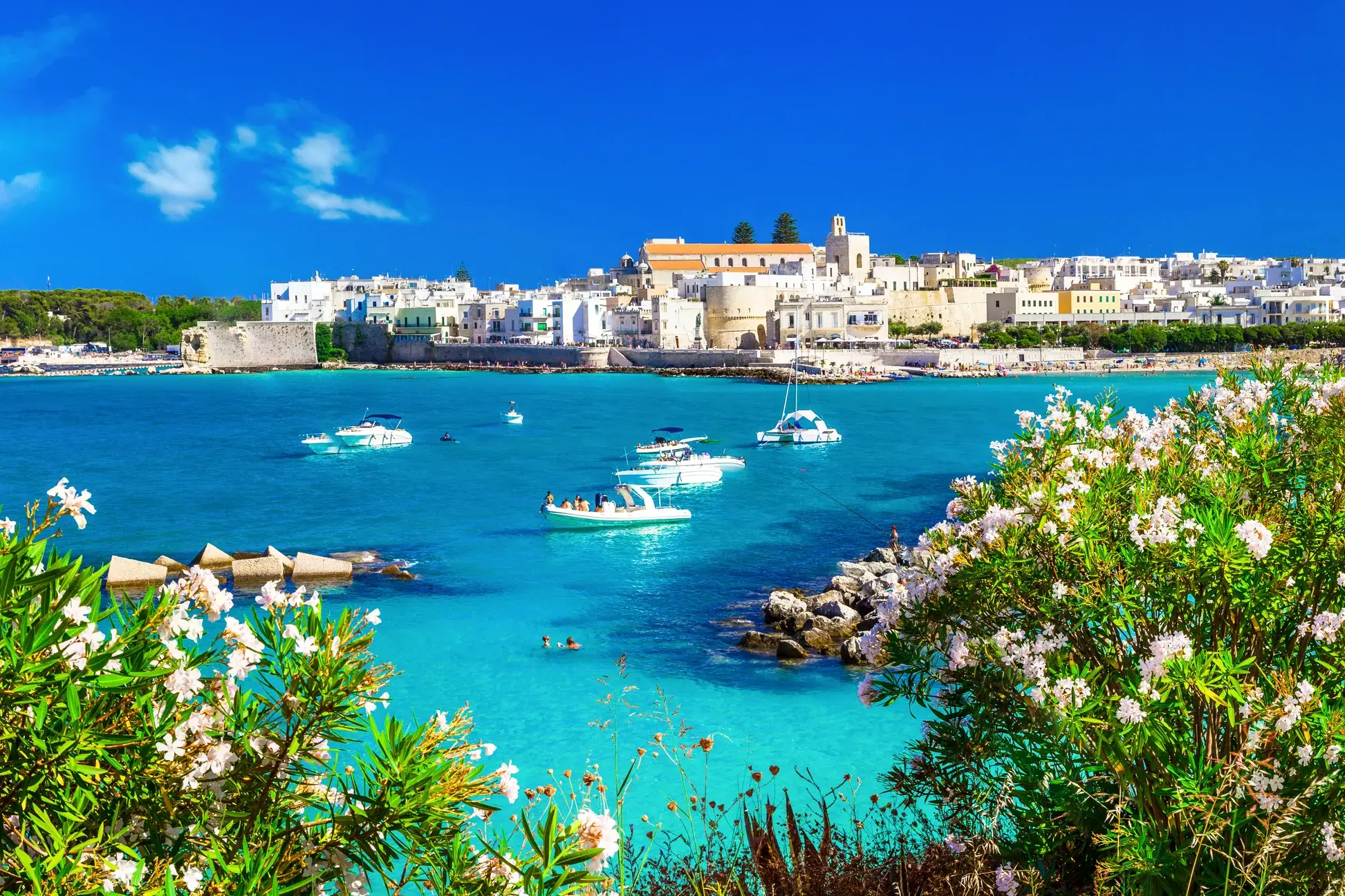 Die weiße Altstadt von Otranto in Apulien thront über der Bucht mit türkisblauem Wasser und kleinen Booten.