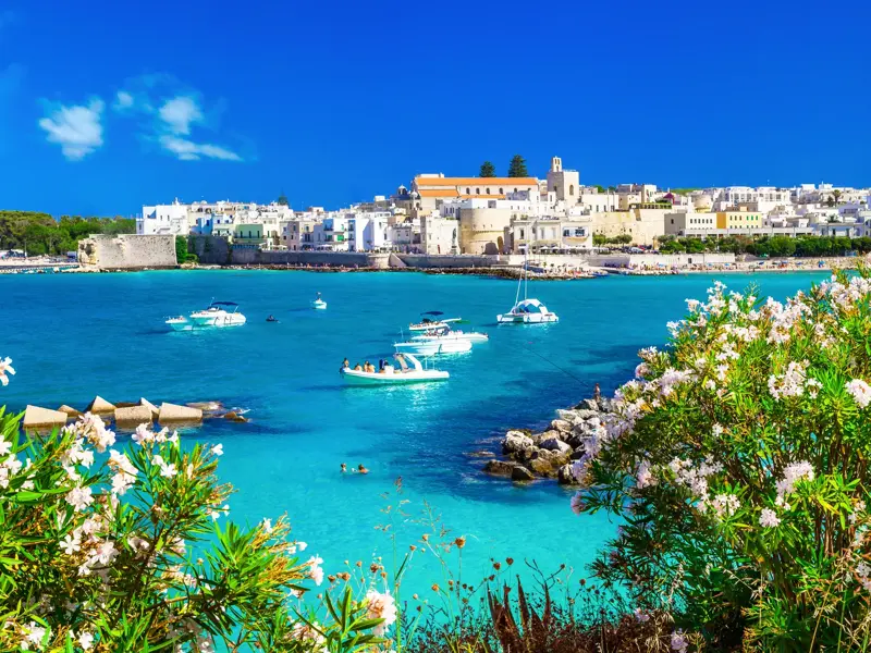 Die weiße Altstadt von Otranto in Apulien thront über der Bucht mit türkisblauem Wasser und kleinen Booten.