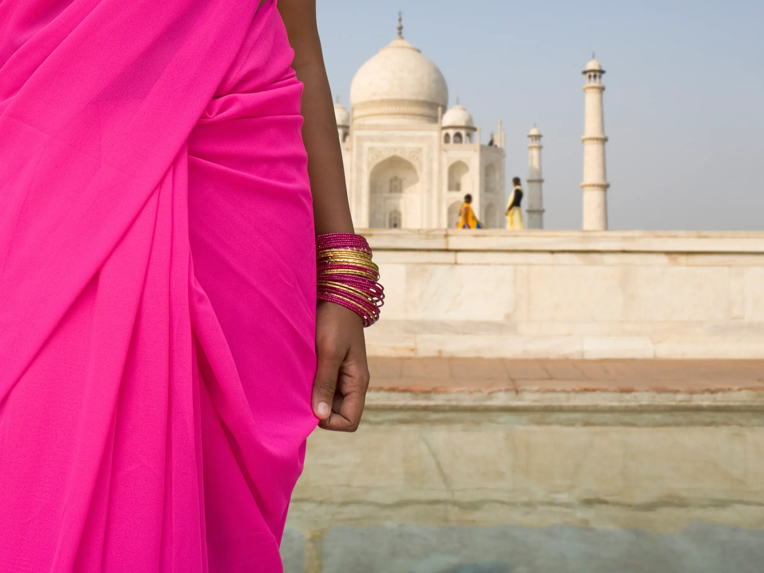 Eine Frau in einem leuchtend pinken Sari und traditionellen Armreifen vor der Kulisse des weltberühmten Taj Mahal in Agra.