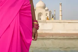 Eine Frau in einem leuchtend pinken Sari und traditionellen Armreifen vor der Kulisse des weltberühmten Taj Mahal in Agra.