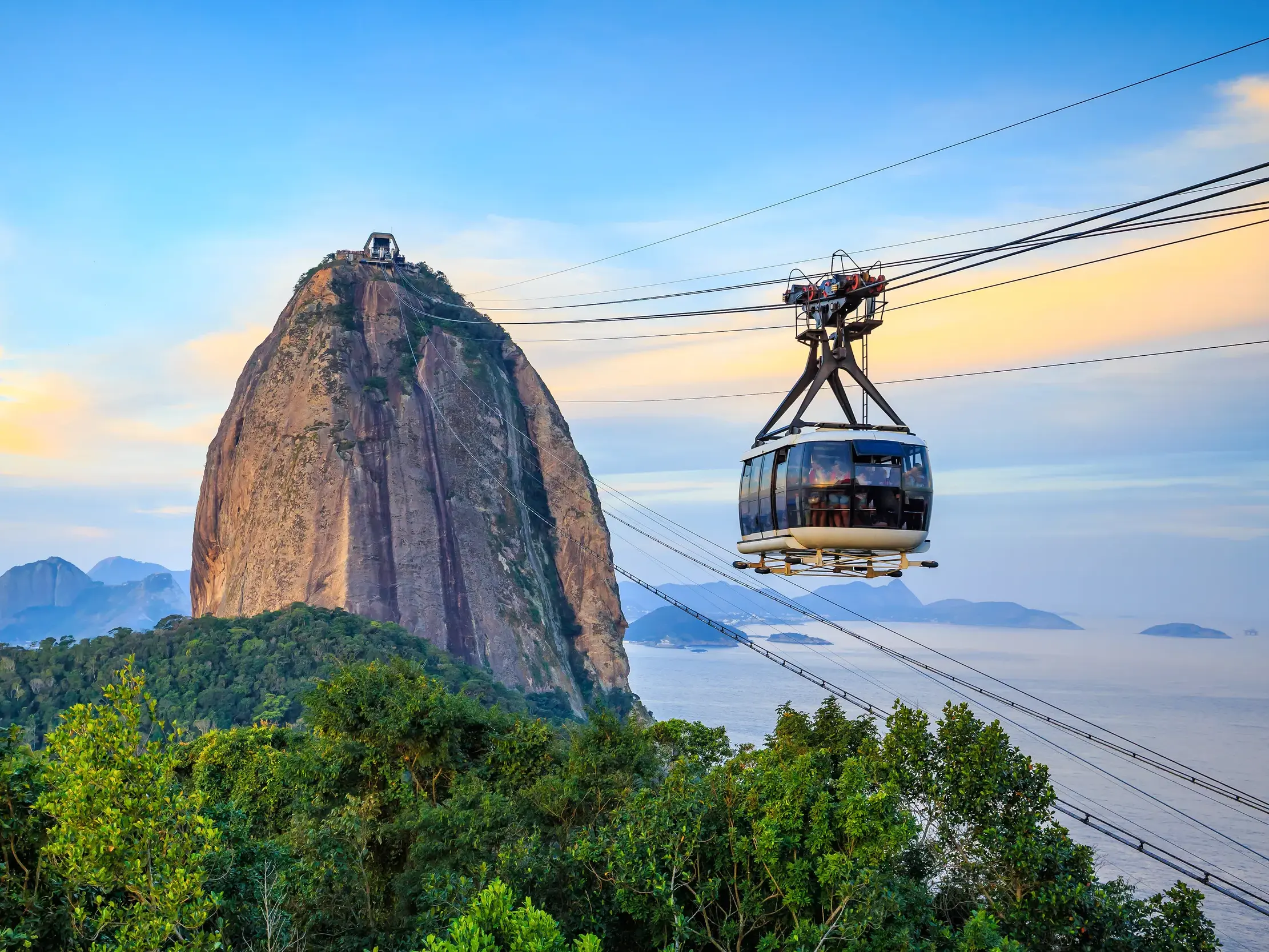 Eine Seilbahngondel schwebt vor dem imposanten Zuckerhut in Rio de Janeiro über tropischem Wald und der Bucht.