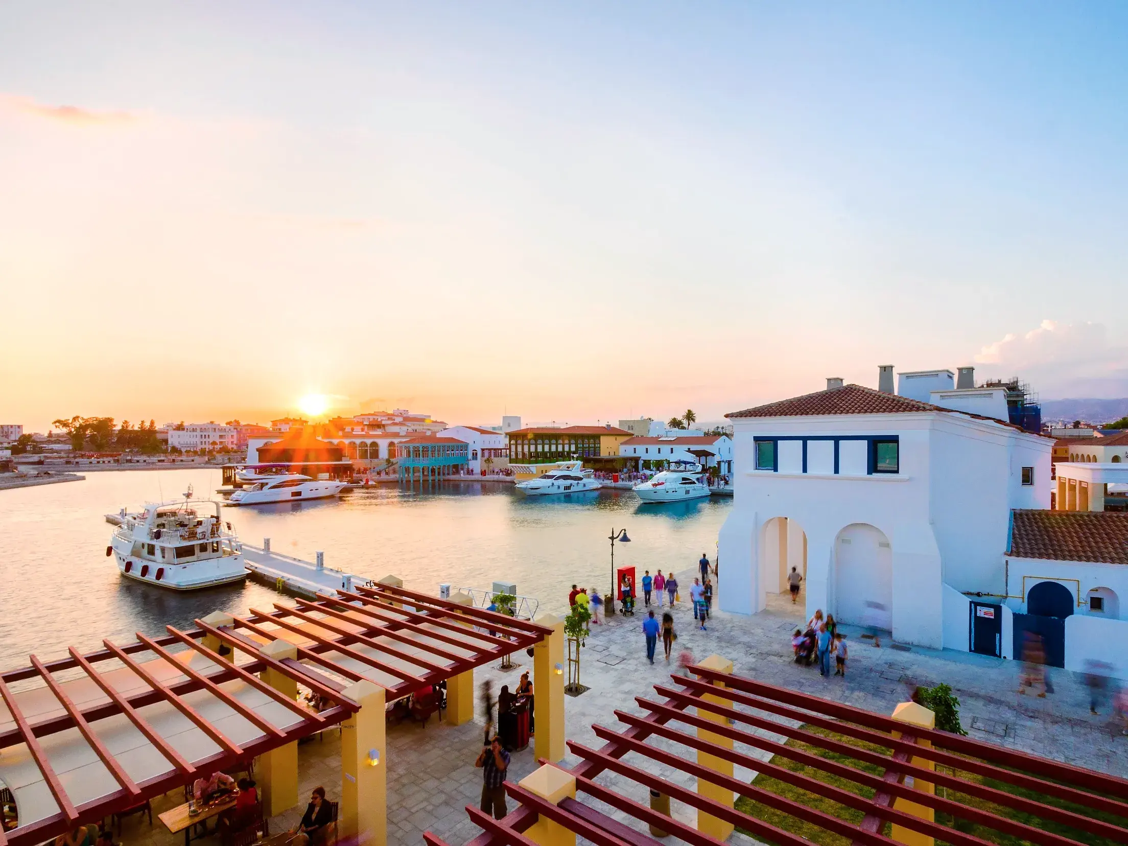 Die moderne Limassol Marina auf Zypern bei Sonnenuntergang, mit Yachten im Hafen und Menschen an der Uferpromenade.