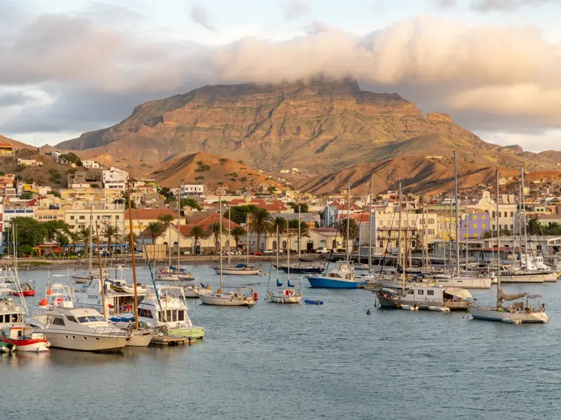 Zahlreiche Boote und Segeljachten im Hafen von Mindelo auf São Vicente, im Hintergrund die bunten Häuser der Stadt und ein Berg.