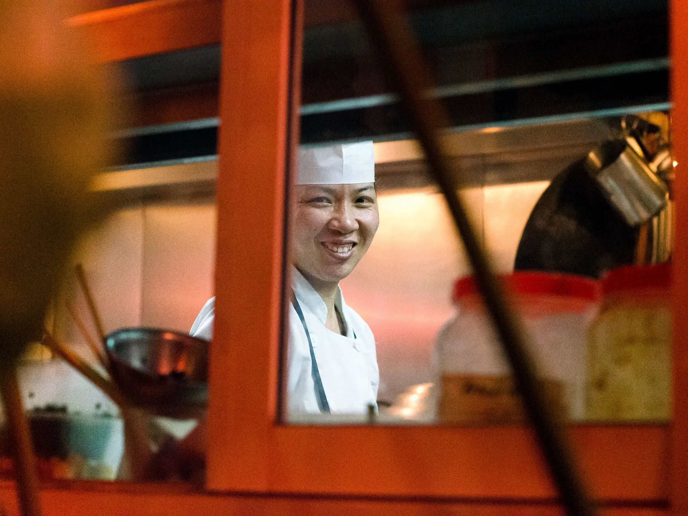 Freundliche vietnamesische Köchin in einer Garküche in Hanoi lächelt durch die orangefarbene Serviceklappe.