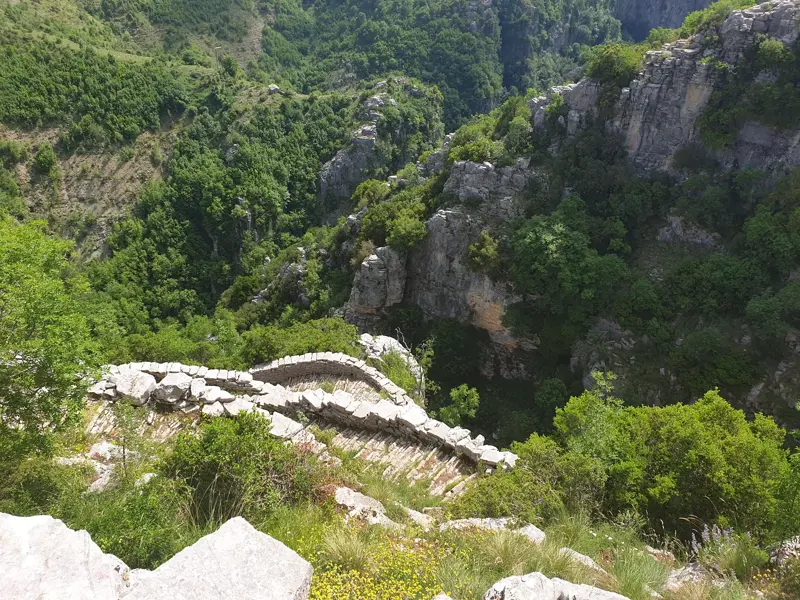 Historischer Steinweg am Rande der tiefen, grünen Vikos-Schlucht in der abgeschiedenen Zagori-Region Griechenlands.