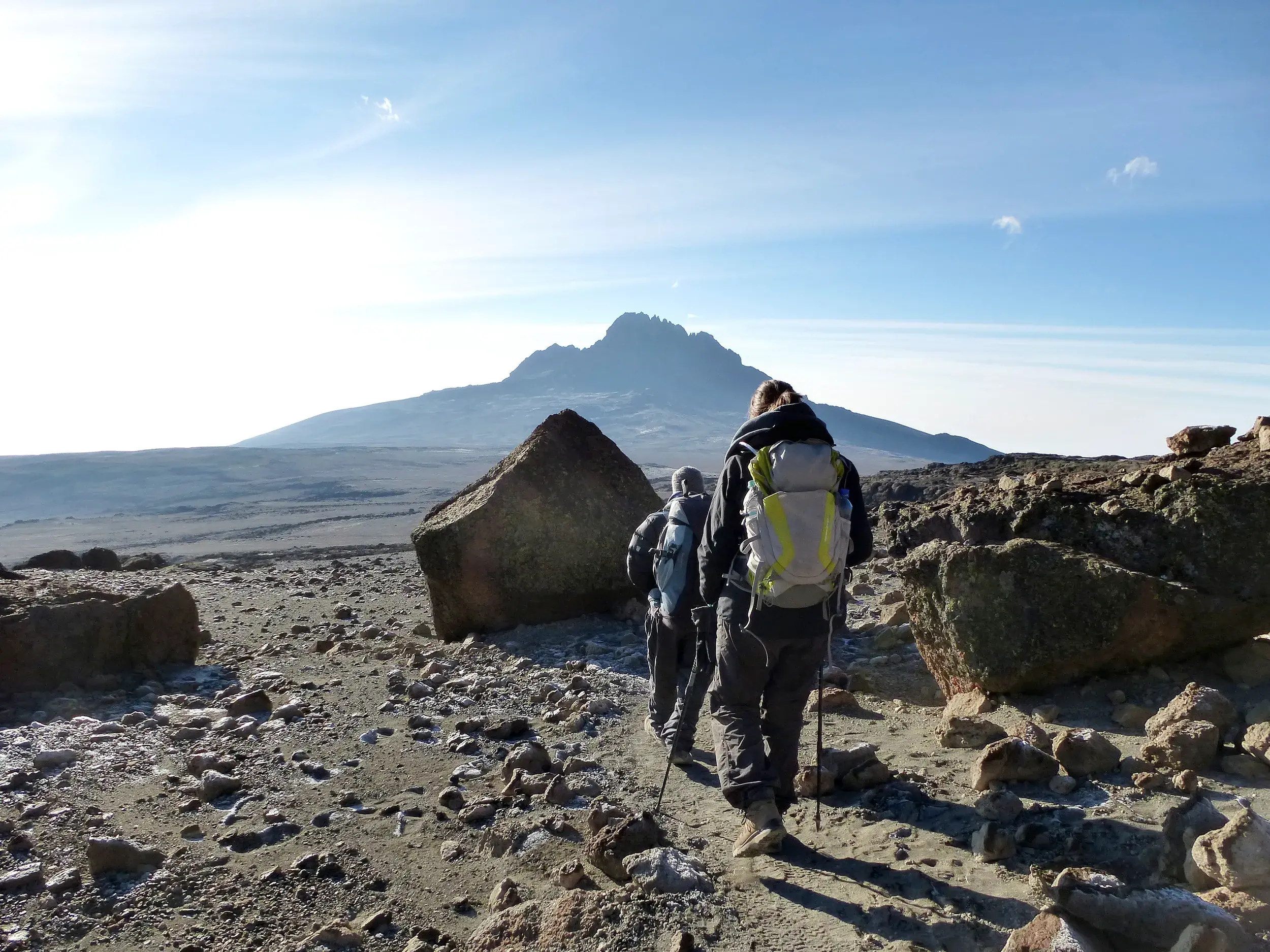 Zwei Wanderer beim Trekking über den Kibo-Sattel am Kilimanjaro mit Blick auf den zerklüfteten Gipfel des Mawenzi.