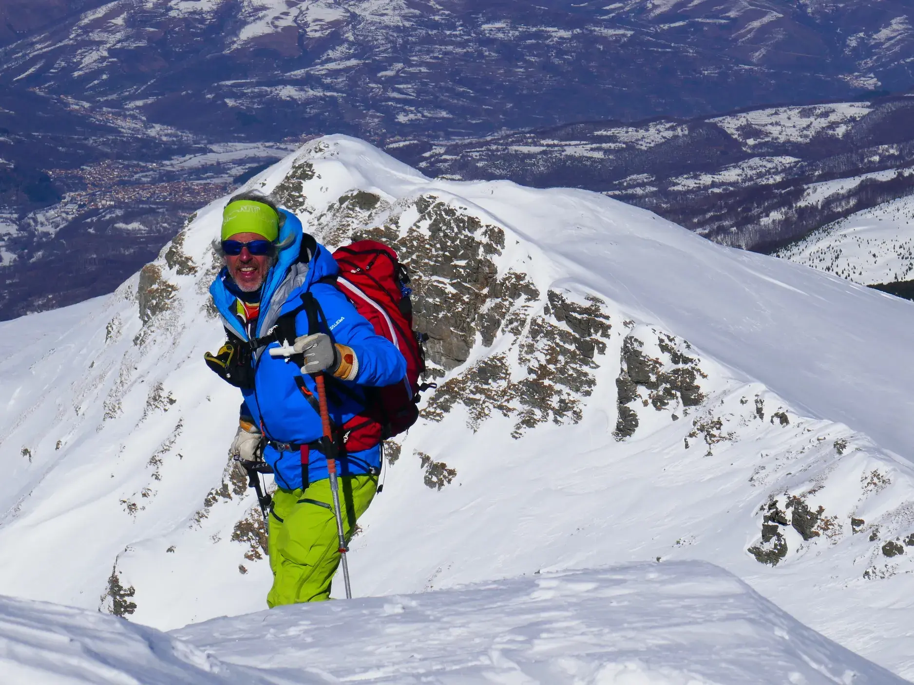 Ein lachender Skifahrer auf einer Skitour im Sharr-Gebirge im Kosovo mit Blick über die weite, verschneite Berglandschaft.