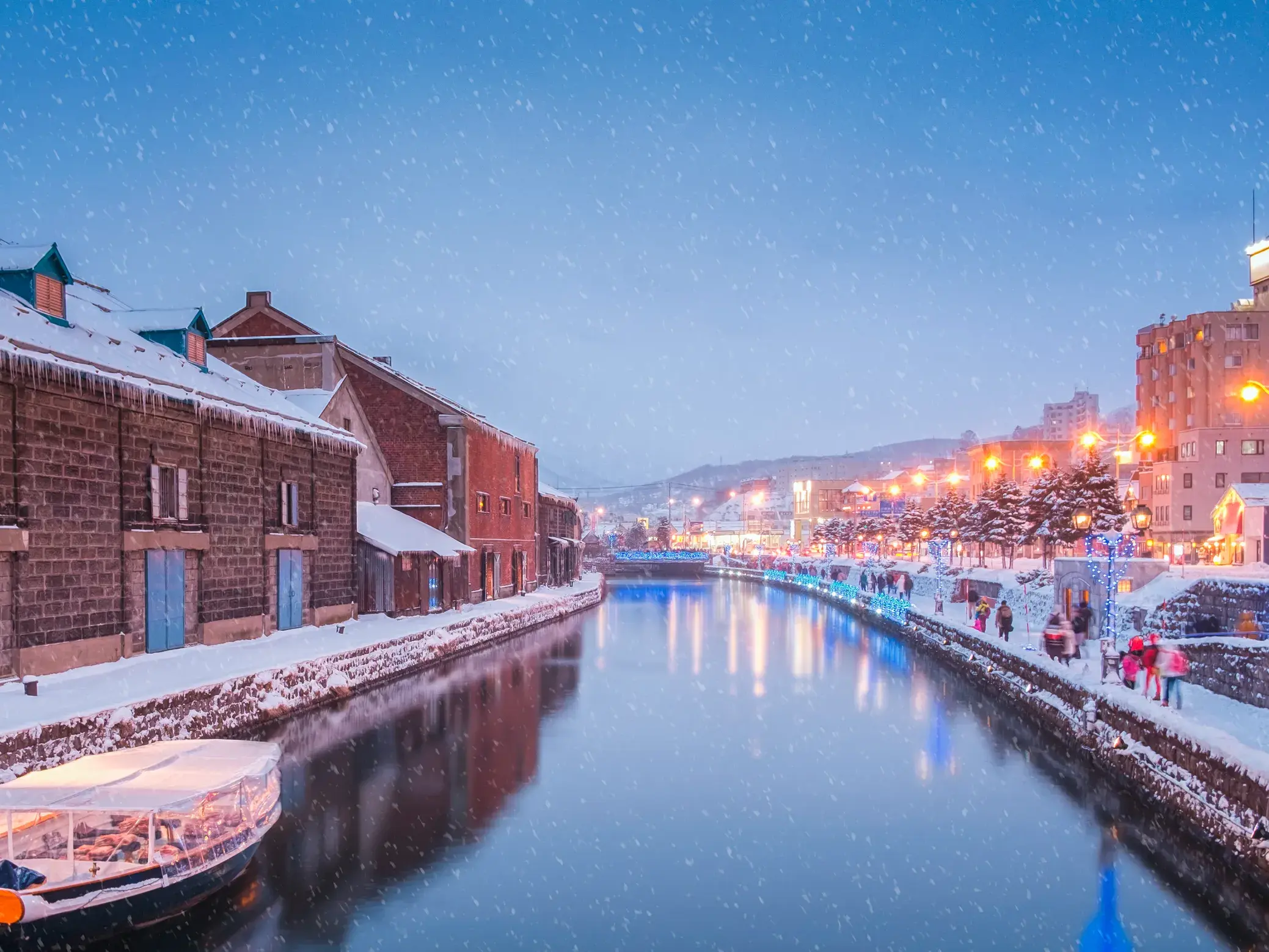 Der verschneite Otaru-Kanal auf Hokkaido in der Abenddämmerung, gesäumt von historischen Lagerhäusern und einer Promenade.