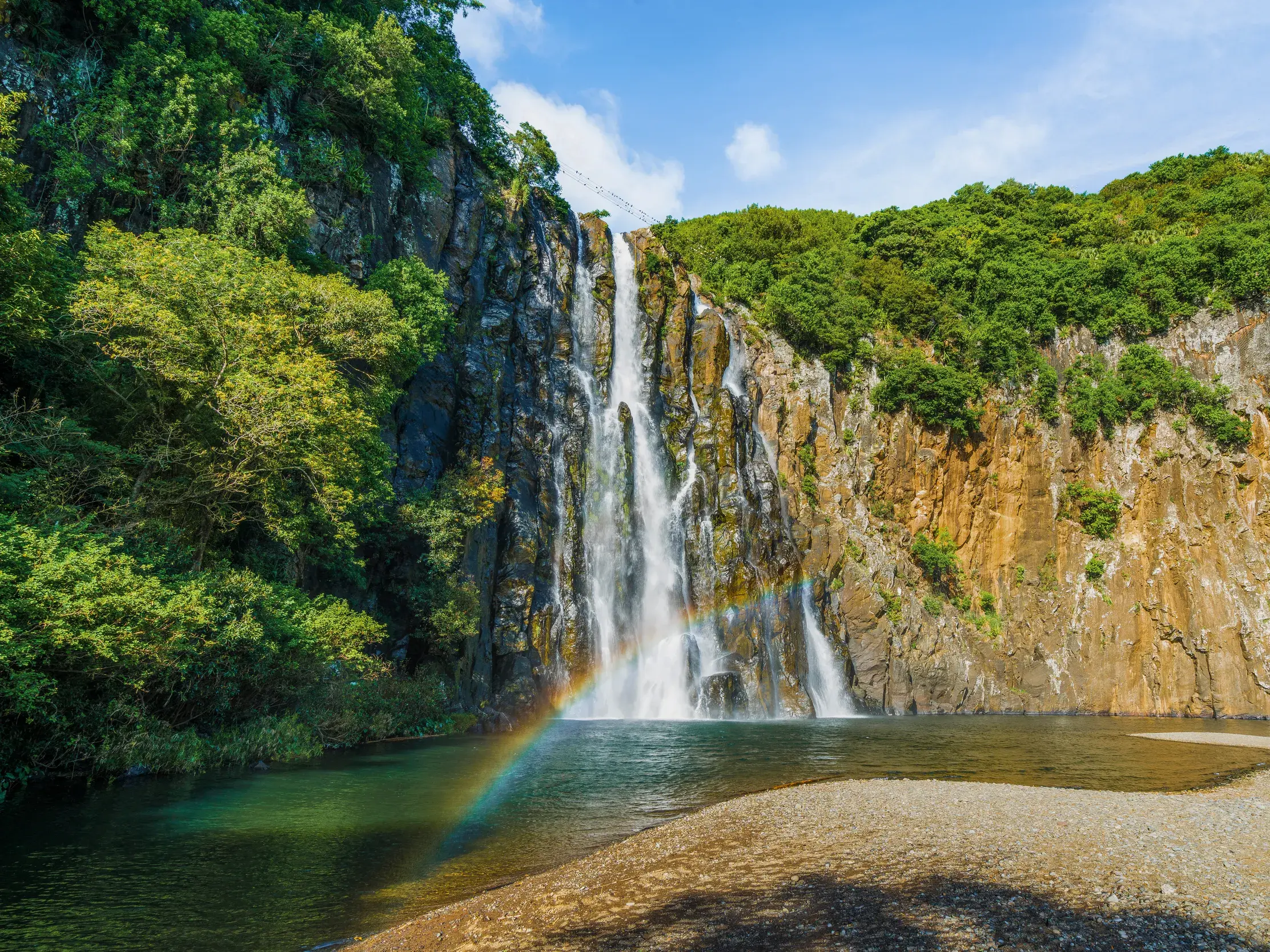 Der beeindruckende Langevin-Wasserfall auf La Réunion stürzt in einen natürlichen Pool, ein Regenbogen leuchtet im Sprühnebel.