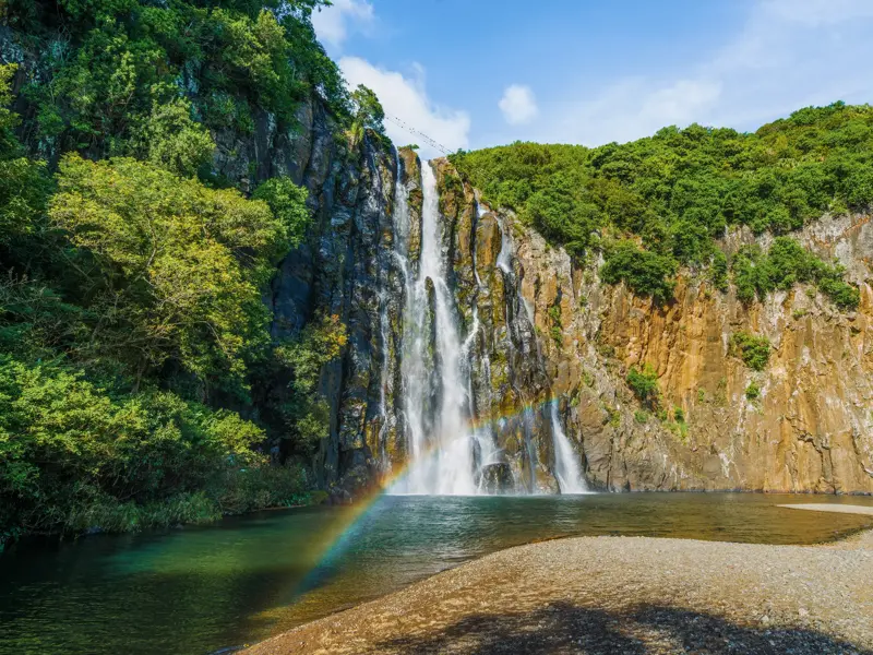 Der beeindruckende Langevin-Wasserfall auf La Réunion stürzt in einen natürlichen Pool, ein Regenbogen leuchtet im Sprühnebel.