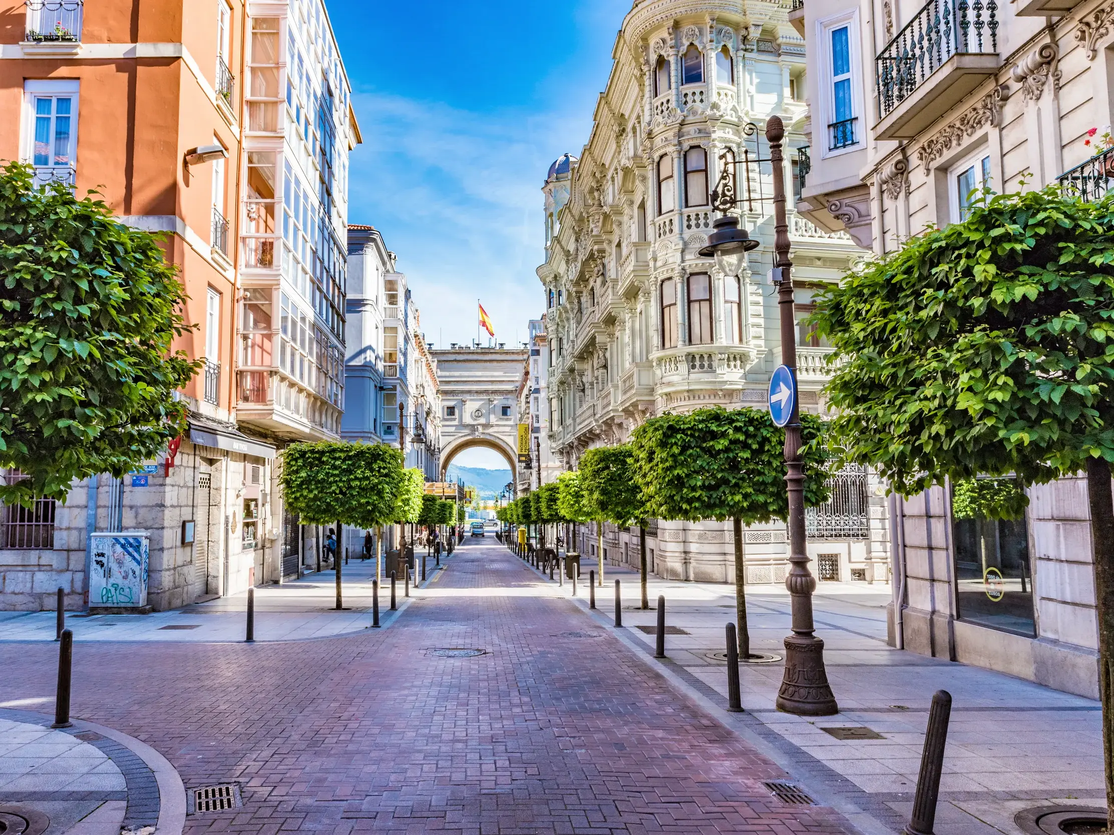 Elegante, von Bäumen gesäumte Straße mit prachtvollen Fassaden und einem Torbogen in der Altstadt von Santander, Kantabrien.