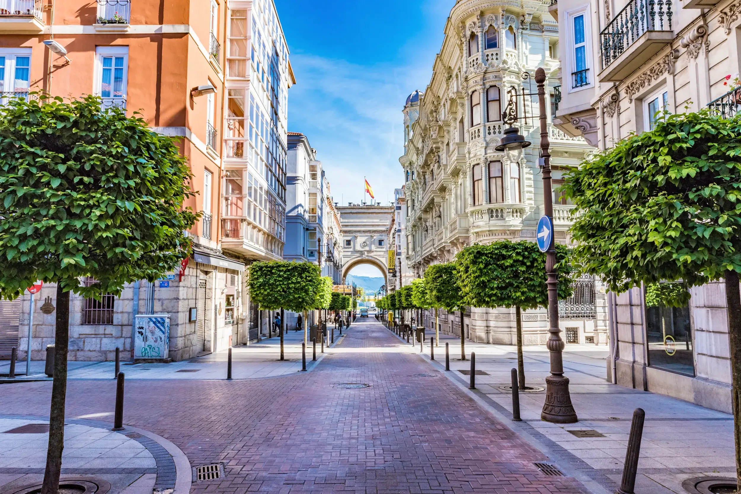 Elegante, von Bäumen gesäumte Straße mit prachtvollen Fassaden und einem Torbogen in der Altstadt von Santander, Kantabrien.