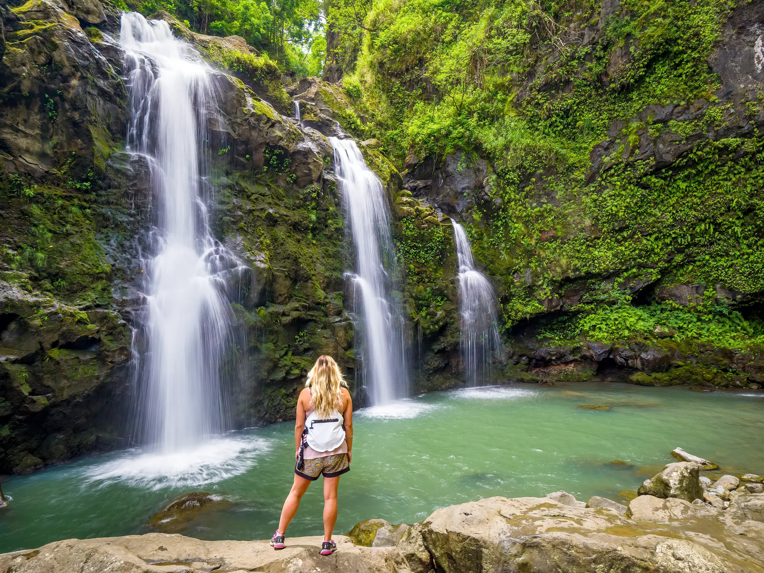 Eine Teilnehmerin einer Studienreise blickt auf die beeindruckenden Wasserfälle auf Kauai, die in ein türkises Becken stürzen.