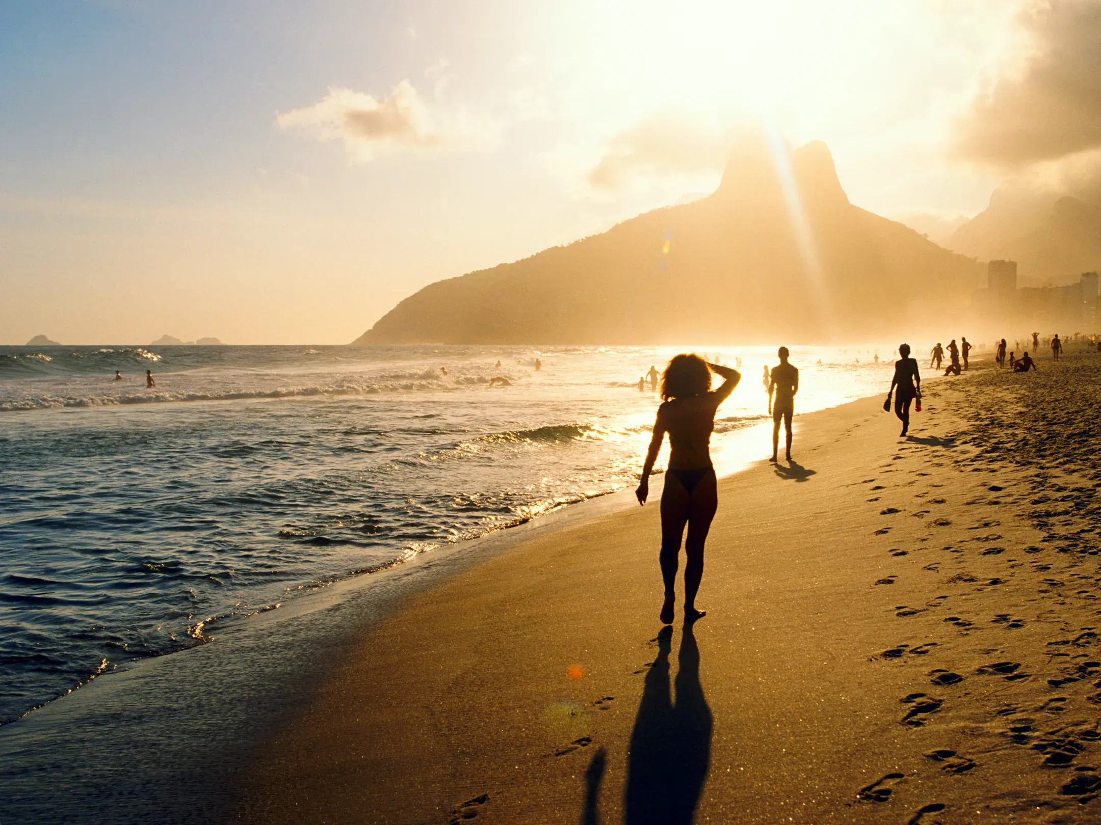 Eine Frau spaziert am Strand von Ipanema im goldenen Sonnenuntergang mit Blick auf den berühmten Berg Dois Irmãos in Rio.