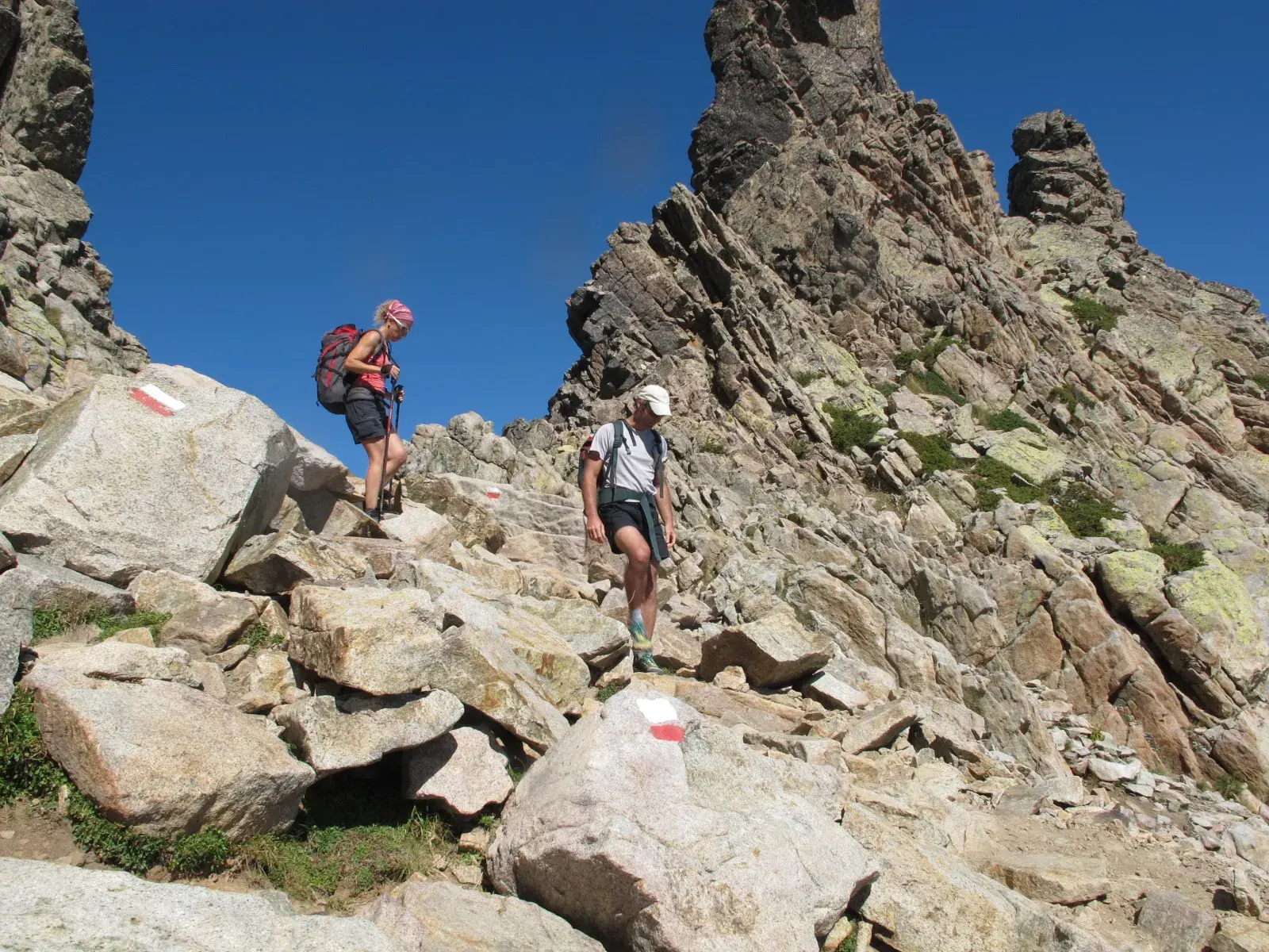 Zwei Wanderer folgen den rot-weißen Markierungen über schroffe Granitfelsen auf einer anspruchsvollen Etappe des GR20 auf Korsika.