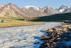 Zeltlager am reißenden Fluss Tsagaan Gol in der Mongolei, im Hintergrund die schneebedeckten Gipfel des Altai-Gebirges.