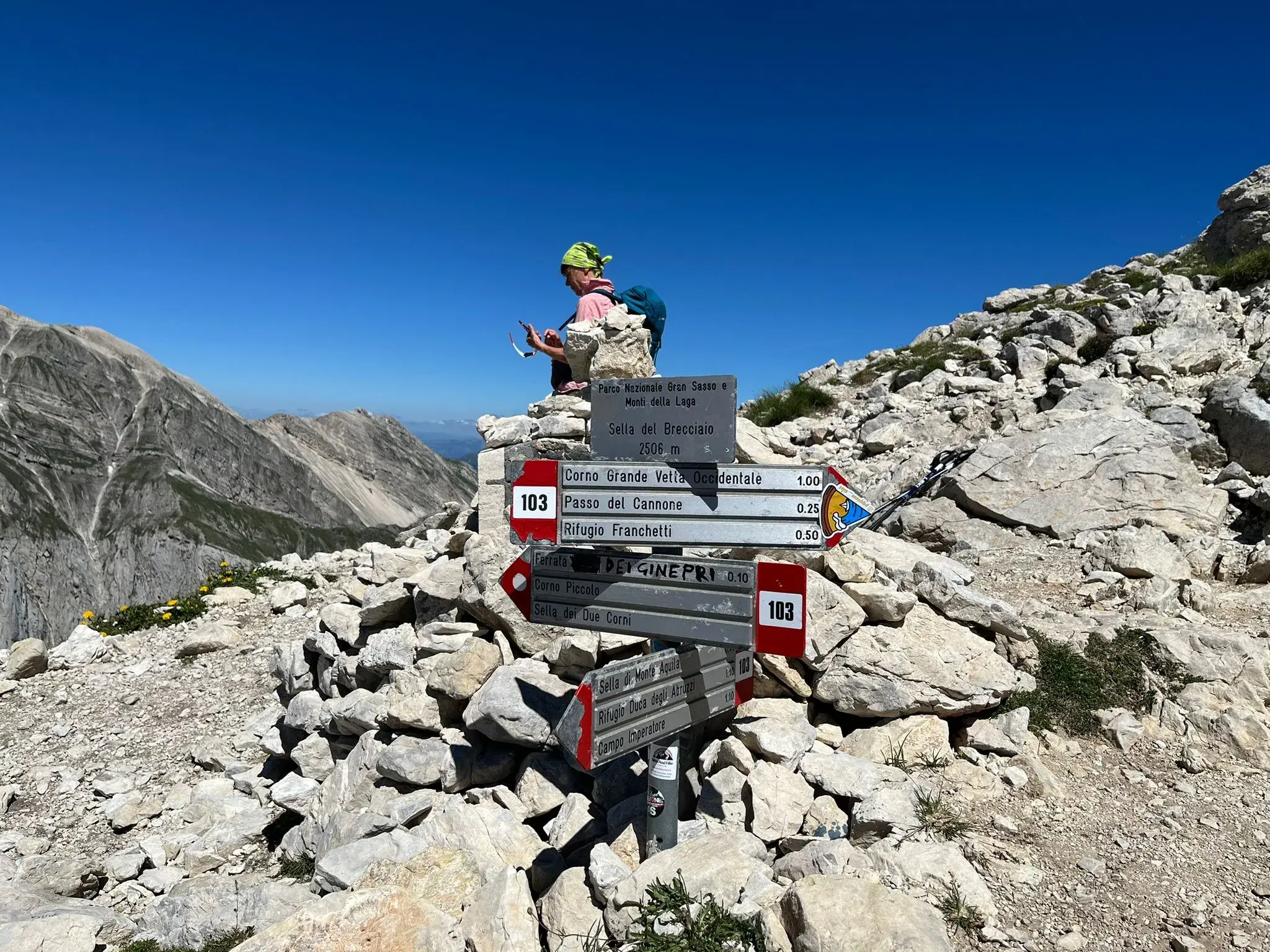 Eine Wanderin macht Rast an einem Wegweiser am Sella del Brecciaio im Nationalpark Gran Sasso e Monti della Laga.