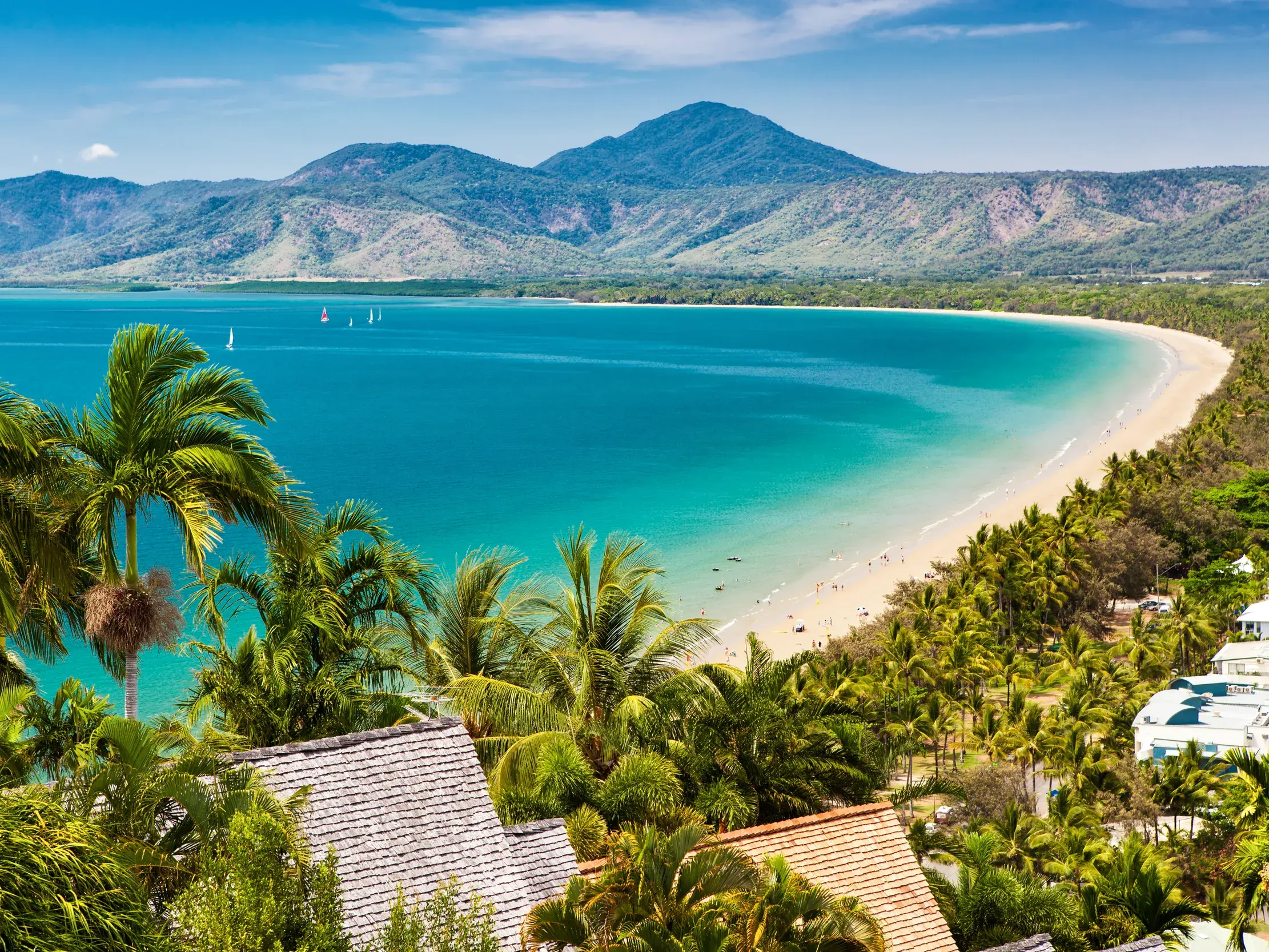 Erhöhte Aussicht auf die Bucht von Port Douglas mit Sandstrand und türkisfarbenem Meer vor der Bergkette des Daintree-Nationalparks.