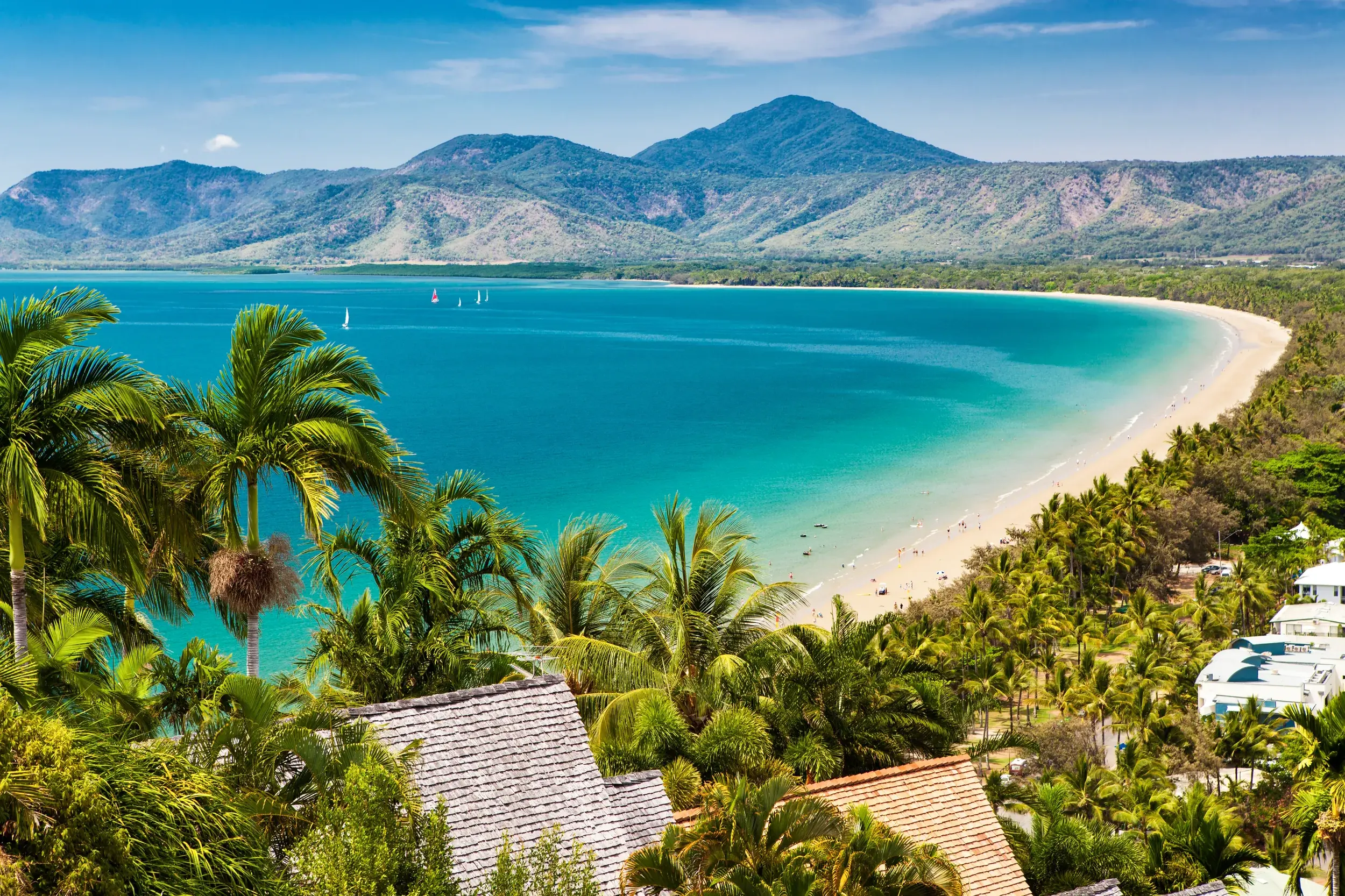 Erhöhte Aussicht auf die Bucht von Port Douglas mit Sandstrand und türkisfarbenem Meer vor der Bergkette des Daintree-Nationalparks.