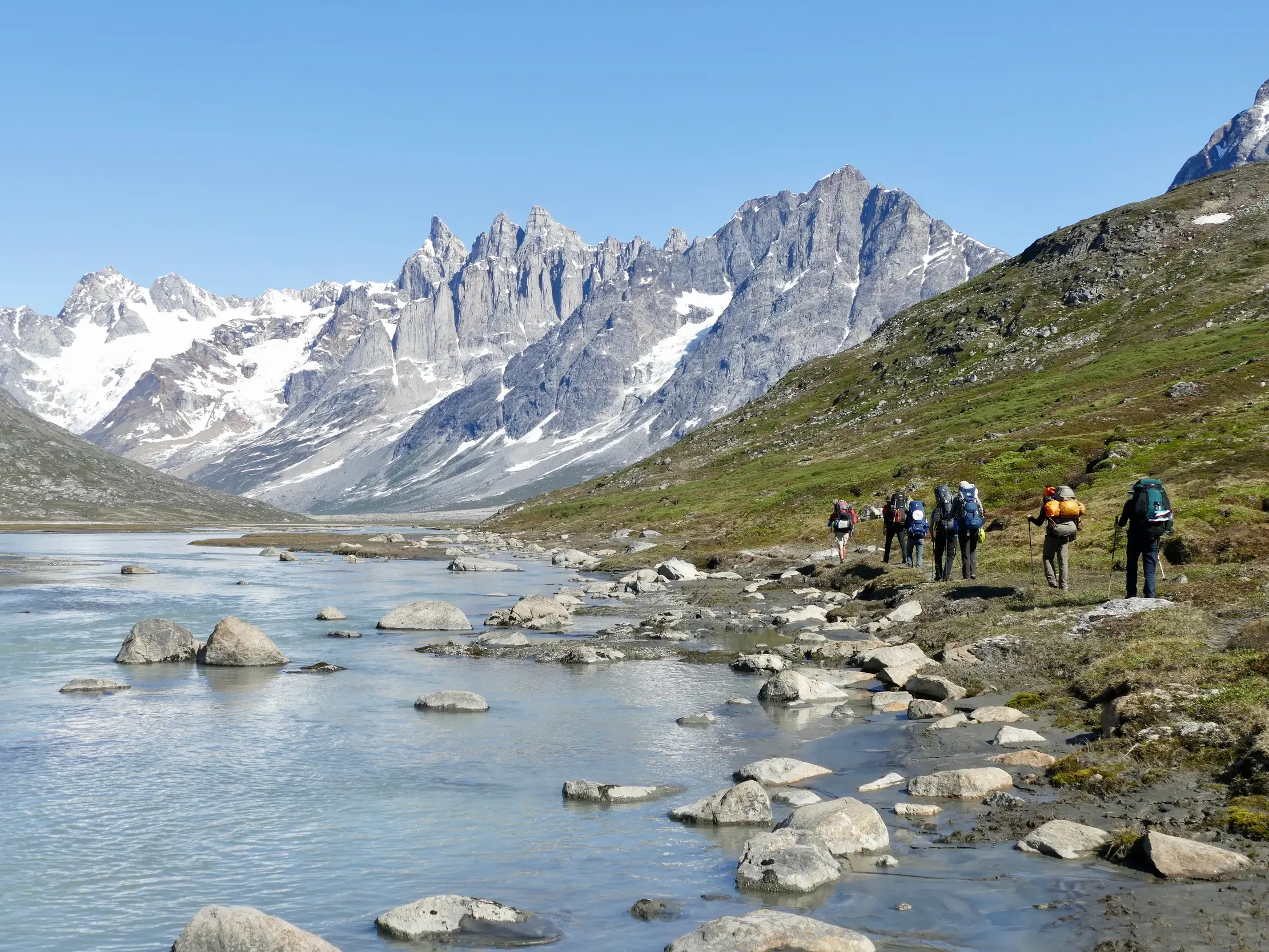 Eine Hauser Reisegruppe beim Trekking am Tasiilaq-Kuua in Ostgrönland mit Blick auf die schneebedeckten Pikkelhuen-Berge.