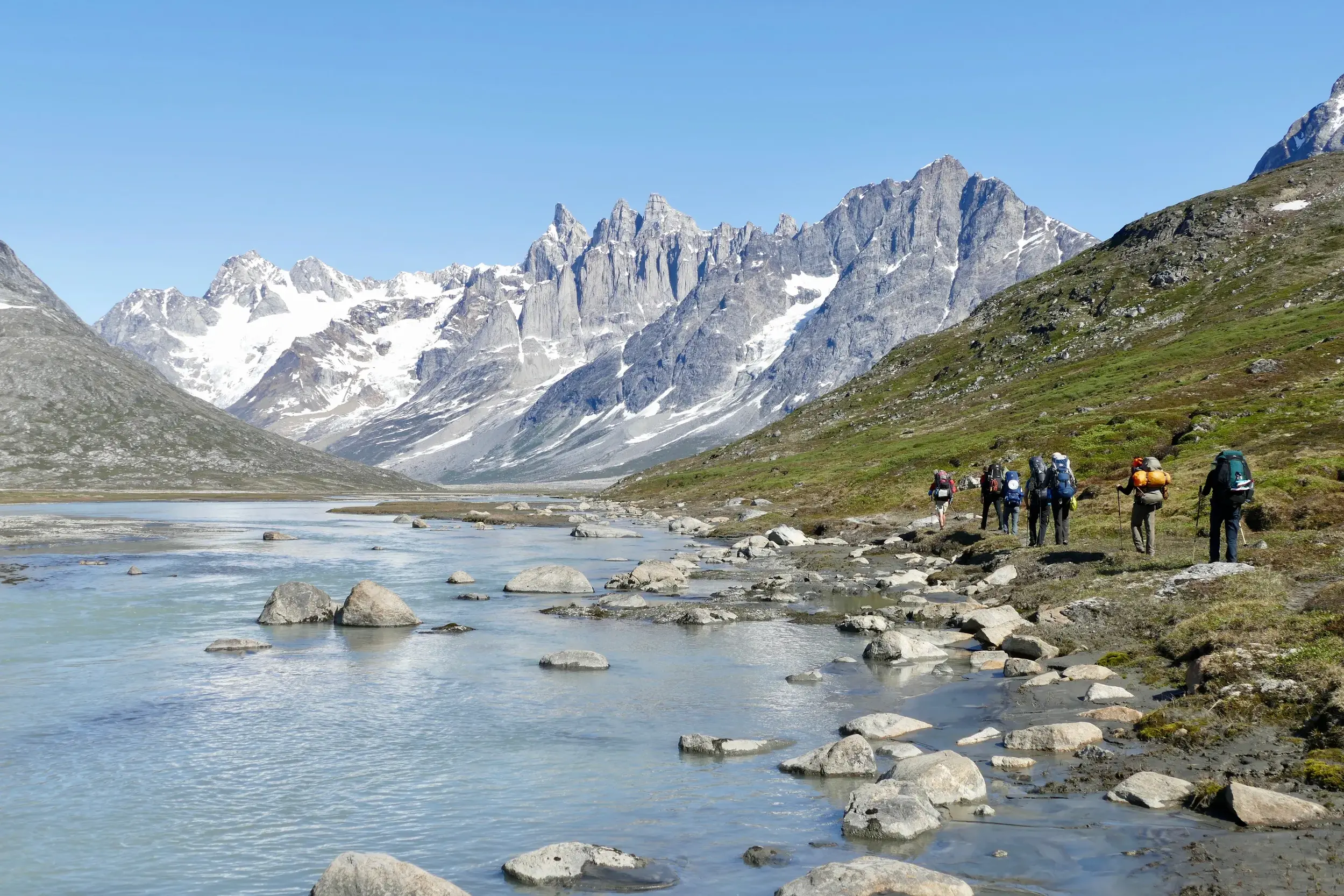 Eine Hauser Reisegruppe beim Trekking am Tasiilaq-Kuua in Ostgrönland mit Blick auf die schneebedeckten Pikkelhuen-Berge.