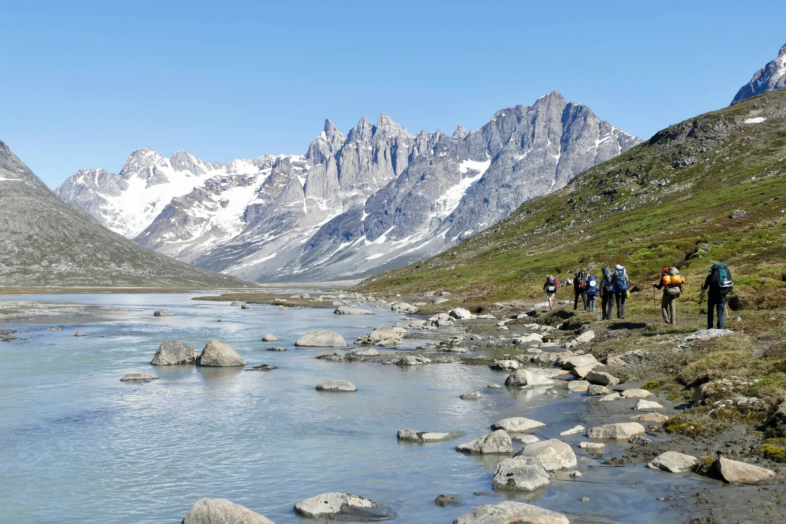 Eine Hauser Reisegruppe beim Trekking am Tasiilaq-Kuua in Ostgrönland mit Blick auf die schneebedeckten Pikkelhuen-Berge.