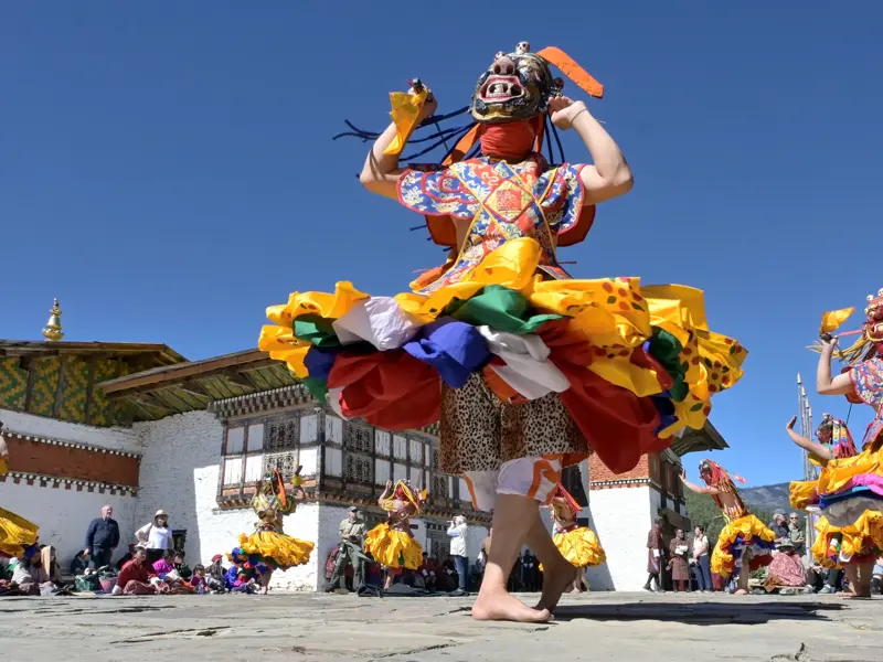 Tänzer in farbenprächtigem Kostüm und Maske beim rituellen Cham-Tanz auf einem Klosterfest in Bhutan.