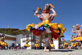 Tänzer in farbenprächtigem Kostüm und Maske beim rituellen Cham-Tanz auf einem Klosterfest in Bhutan.