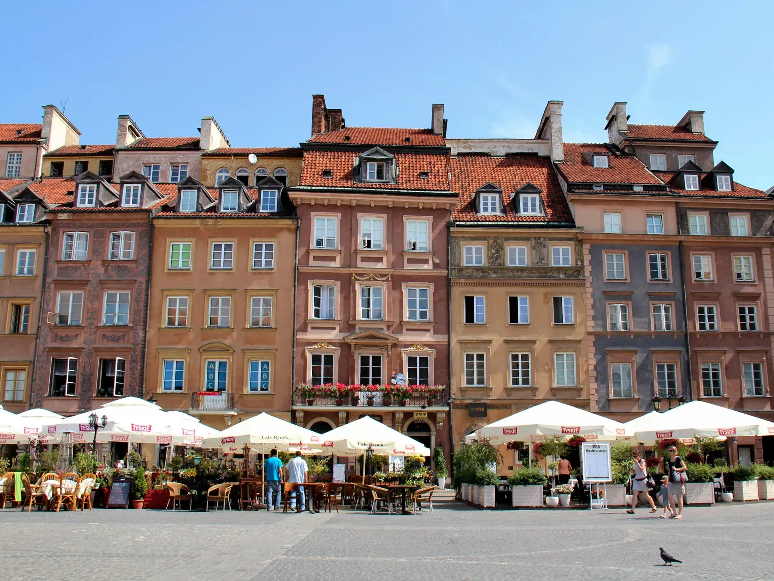 Bunte, historische Patrizierhäuser am Marktplatz der Warschauer Altstadt mit Cafés und Spaziergängern bei Sonnenschein.