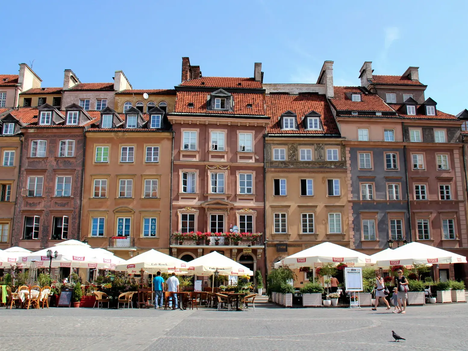 Sonniger Tag am Marktplatz der Warschauer Altstadt mit bunten Patrizierhäusern und belebten Straßencafés.