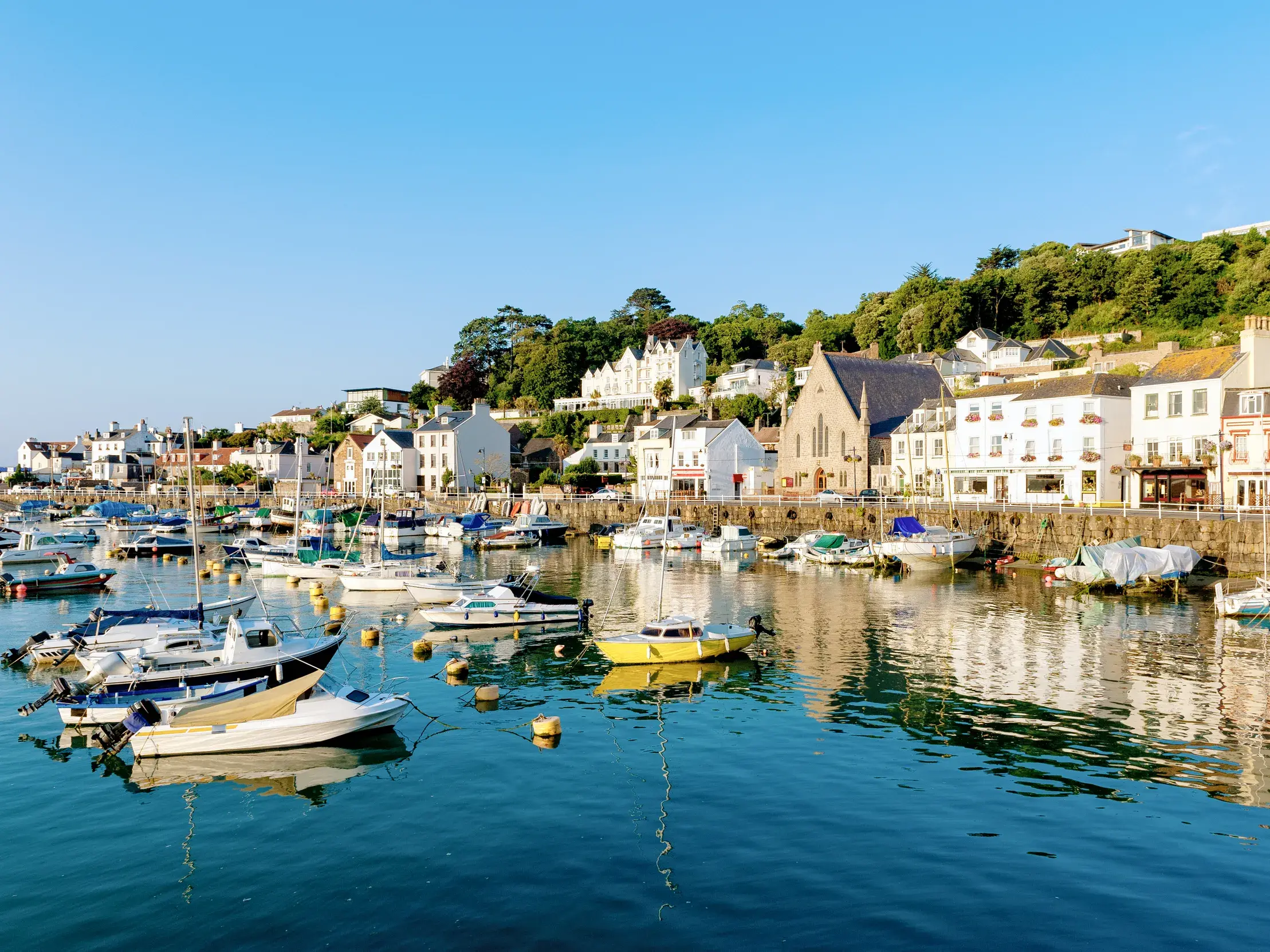 Zahlreiche Segel- und Motorboote im Hafen von St Aubin auf Jersey, dahinter die malerische Stadt an einem grünen Hang.