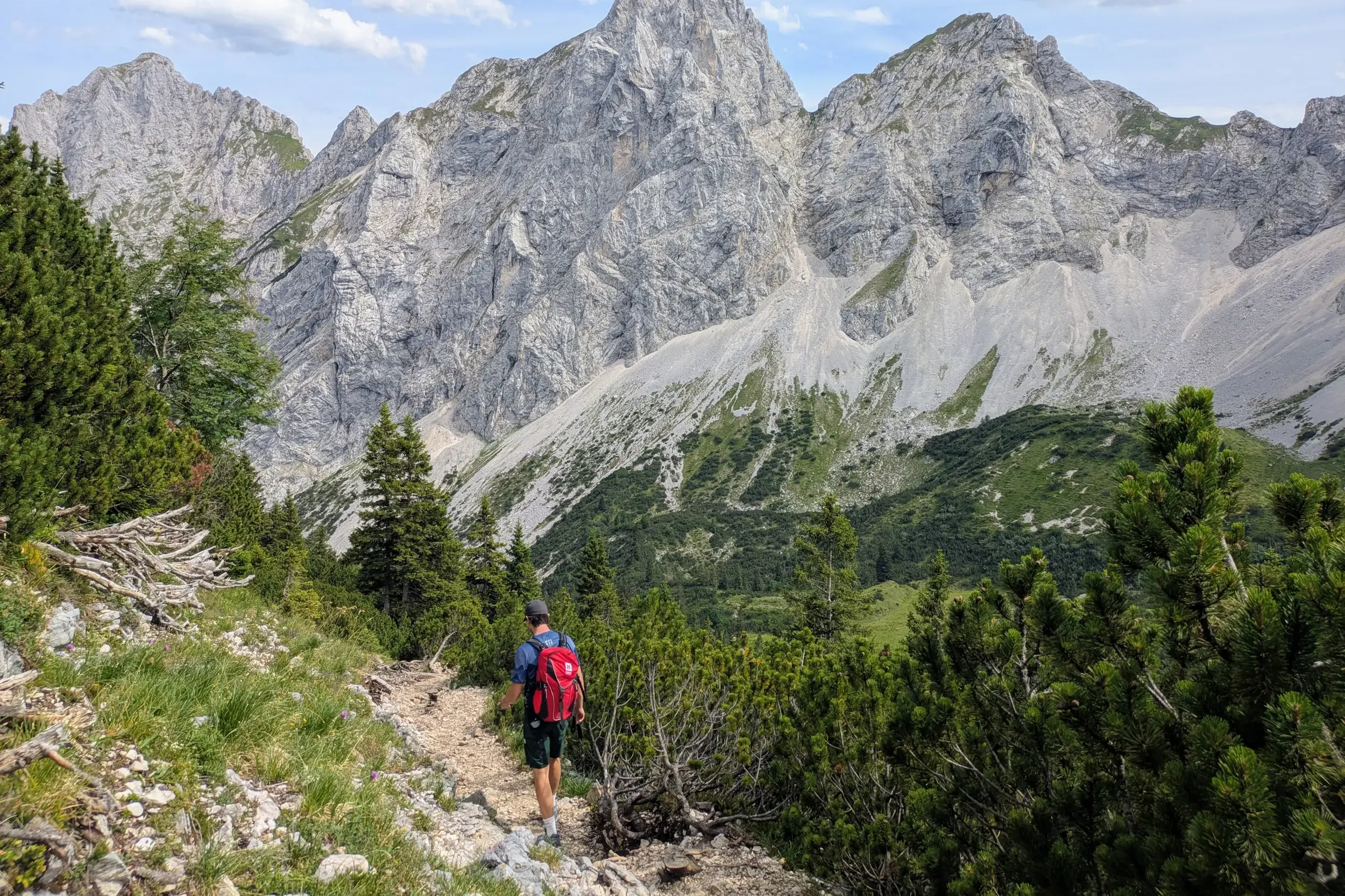 Ein Wanderer mit Rucksack auf einem schmalen Bergpfad mit Blick auf die felsigen Gipfel der Tannheimer Berge im Ostallgäu.