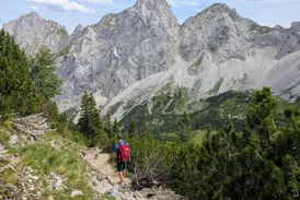 Ein Wanderer mit Rucksack auf einem schmalen Bergpfad mit Blick auf die felsigen Gipfel der Tannheimer Berge im Ostallgäu.