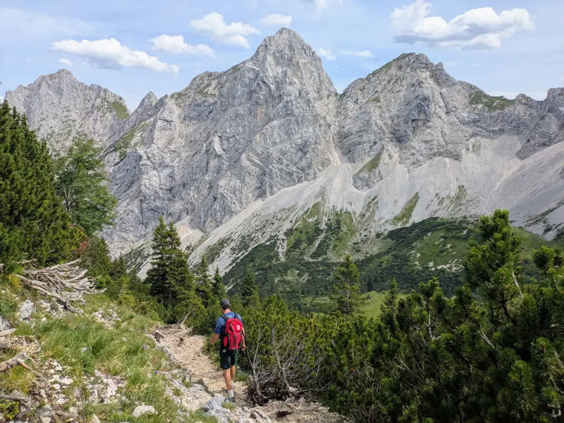 Ein Wanderer mit Rucksack auf einem schmalen Bergpfad mit Blick auf die felsigen Gipfel der Tannheimer Berge im Ostallgäu.