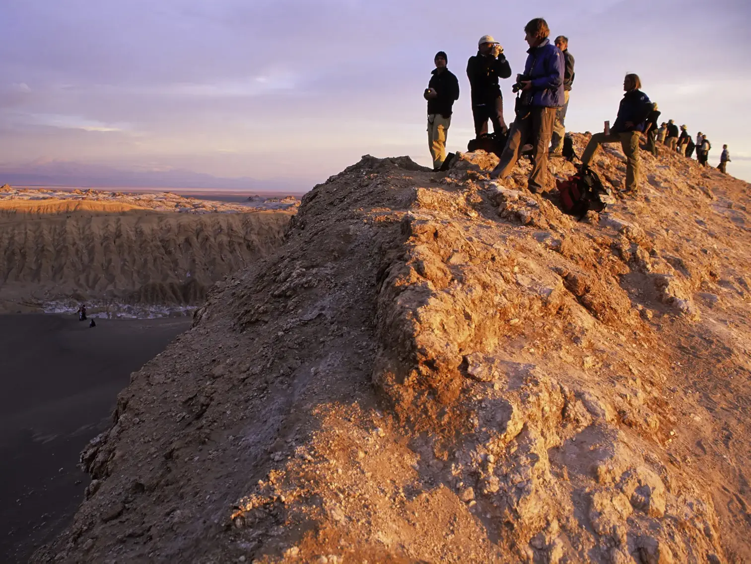 Eine Wandergruppe steht auf einem Felsgrat im Mondtal und beobachtet den Sonnenuntergang über der Atacama-Wüste in Chile.