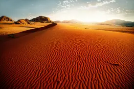 Die untergehende Sonne taucht die geriffelten, roten Sanddünen und Felsformationen im Wadi Ram in ein warmes Licht.