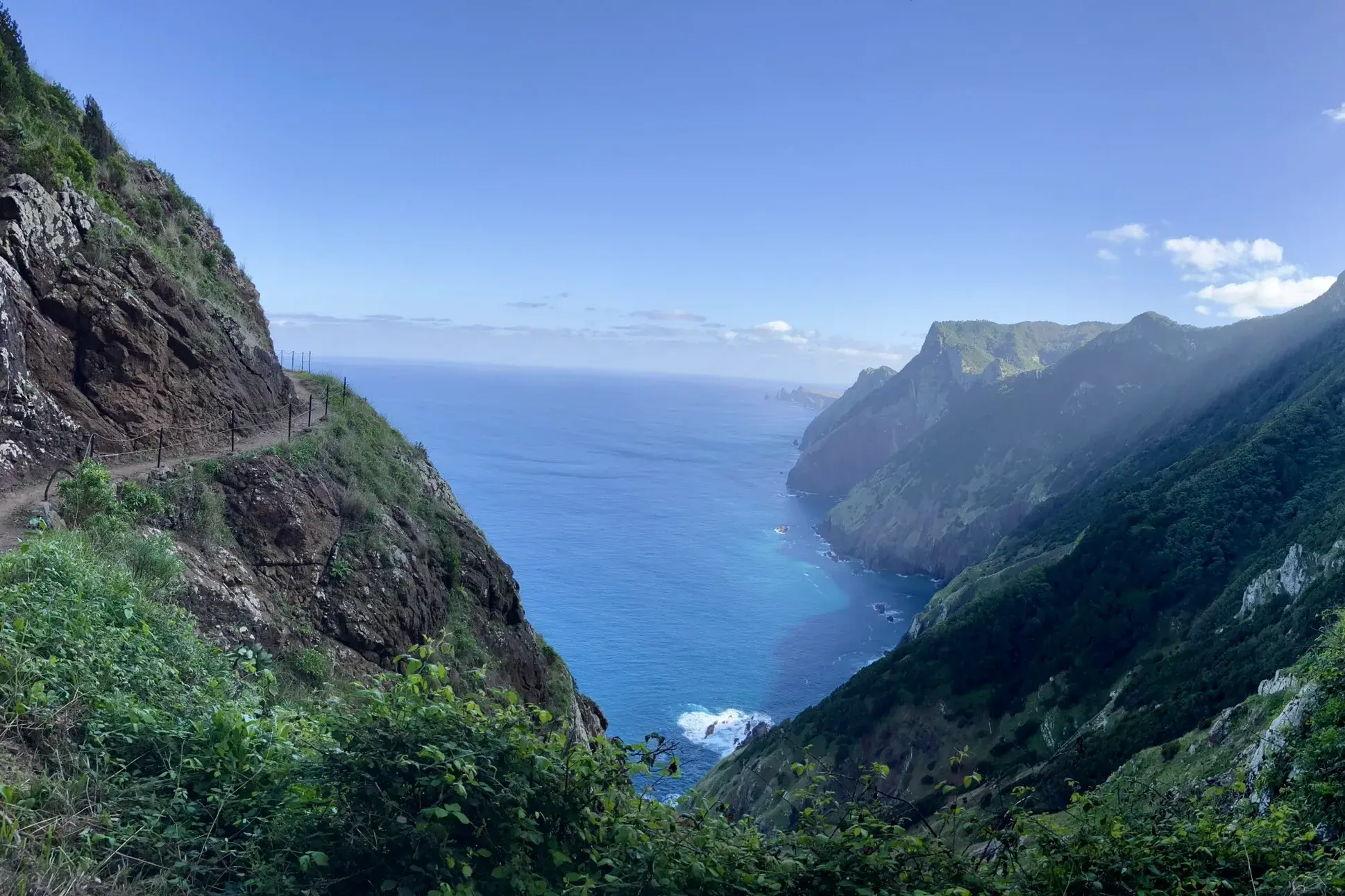 Schmaler Wanderpfad am Boca do Risco, der sich an Madeiras grüner Steilküste mit Blick auf den blauen Atlantik schlängelt.