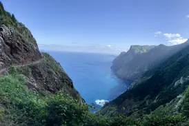 Schmaler Wanderpfad am Boca do Risco, der sich an Madeiras grüner Steilküste mit Blick auf den blauen Atlantik schlängelt.