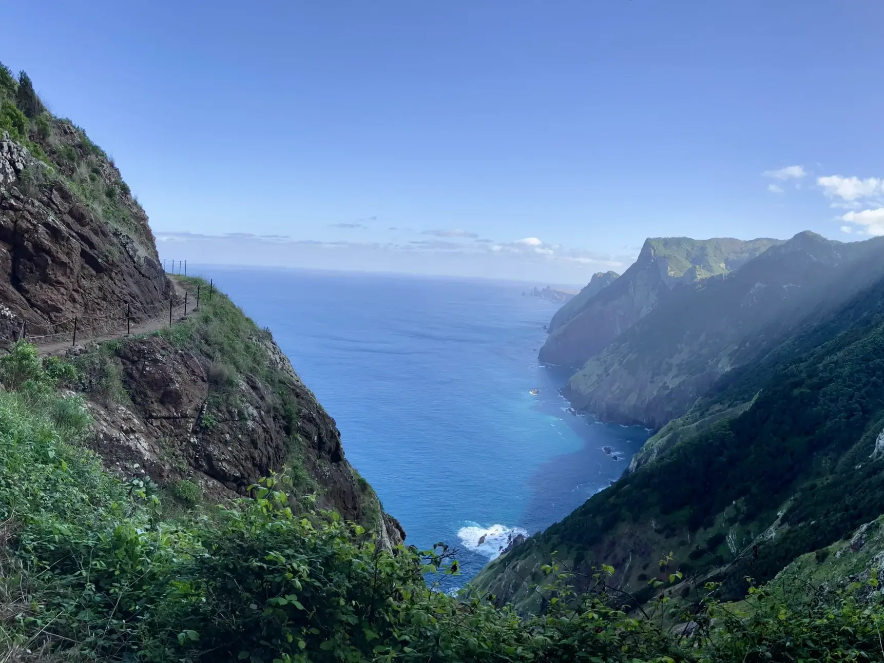 Schmaler Wanderpfad entlang der grünen Steilküste Boca do Risco auf Madeira mit weitem Blick auf den blauen Atlantik.