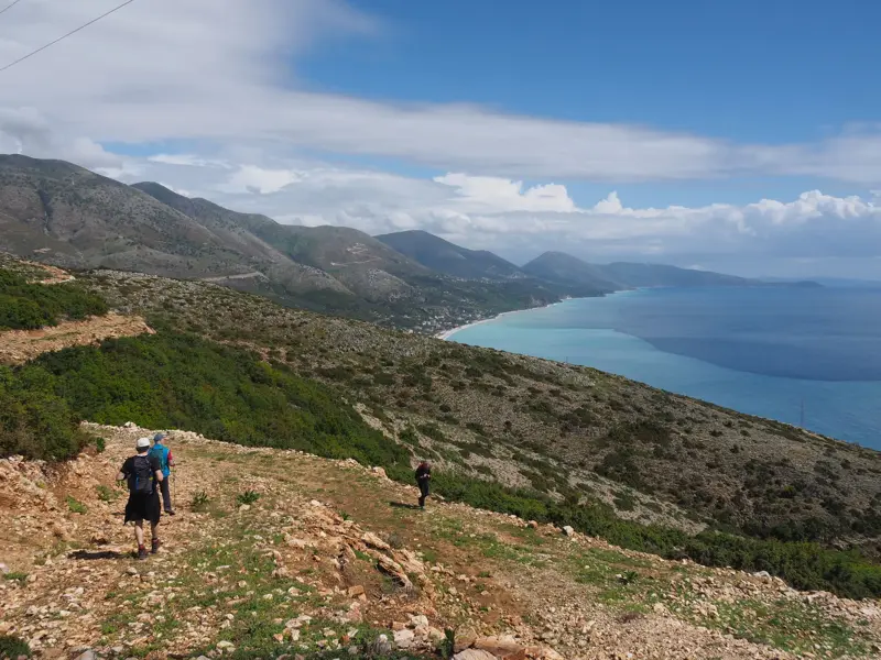 Eine kleine Wandergruppe beim Trekking auf einem Bergpfad hoch über der türkisfarbenen Küste der Albanischen Riviera.