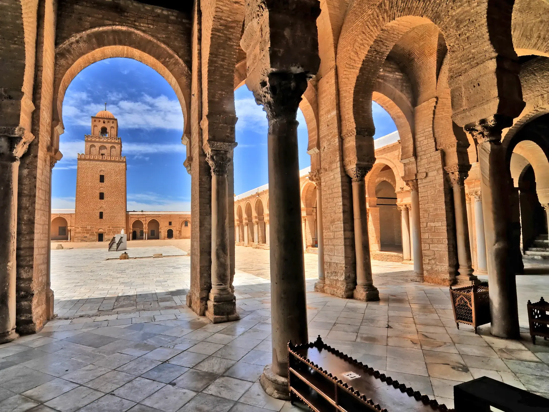 Blick durch die Rundbögen einer Arkade auf den Innenhof und das Minarett der Großen Moschee von Kairouan (UNESCO), ein Highlight dieser Studienreise durch Tunesien.