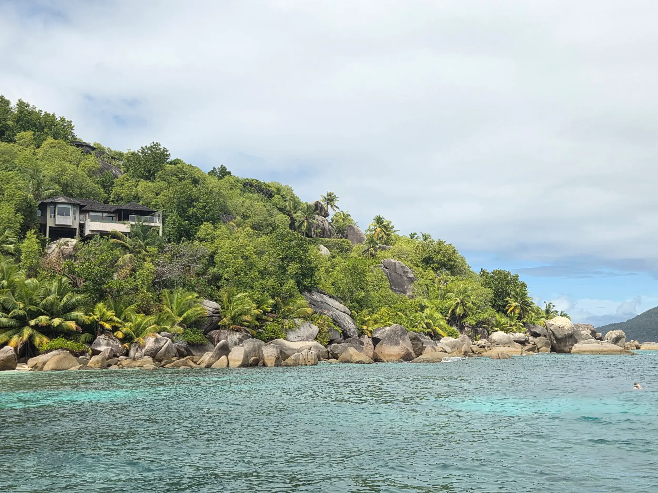 Tropische Küstenlandschaft auf Mahé, Seychellen, mit Granitfelsen, Palmen und türkisfarbenem Meer bei einer Bootstour.