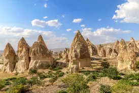 Spitze, beige Tuffsteinkegel, bekannt als Feenkamine, in der weiten, bizarren Landschaft von Kappadokien unter blauem Himmel.