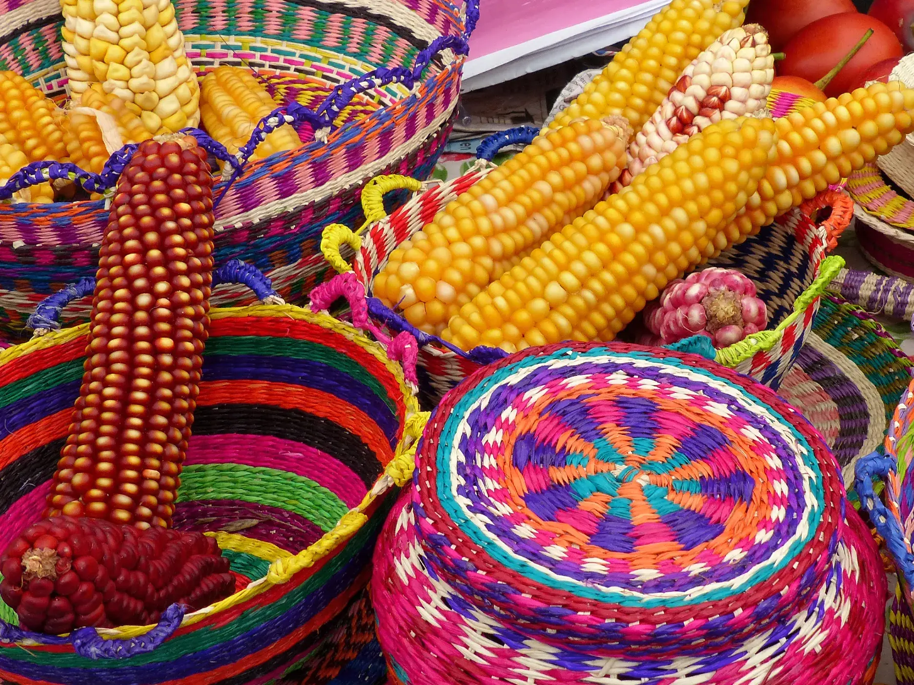 Gelbe und rote Maiskolben in bunten, handgeflochtenen Körben auf dem berühmten Indiomarkt von Otavalo in Ecuador.