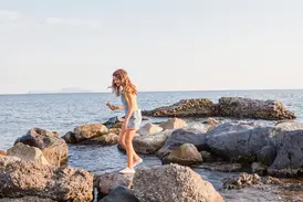 Lächelndes Mädchen mit Eis balanciert auf Felsen am Golf von Neapel, im Hintergrund die sonnige Insel Capri.
