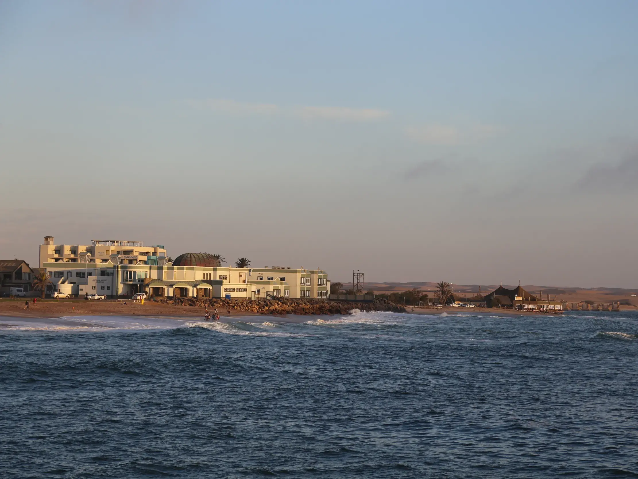 Wellen des Atlantiks an der Küste von Swakopmund in Namibia mit Hotels am Strand und der Wüste im Hintergrund.