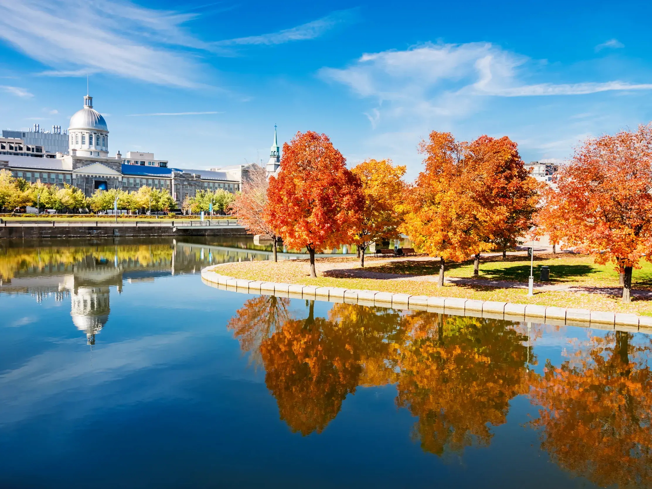 Das Marché Bonsecours in Montréal spiegelt sich im Wasser, umgeben von Bäumen im leuchtenden Herbstlaub des Indian Summer.