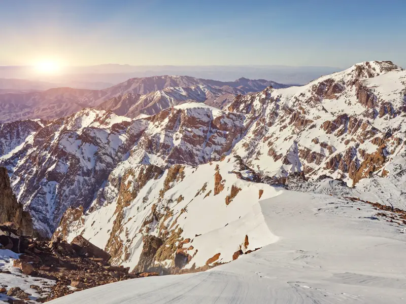 Panoramablick vom Gipfel des Toubkal auf die verschneiten Berge des Hohen Atlas in Marokko bei Sonnenaufgang.